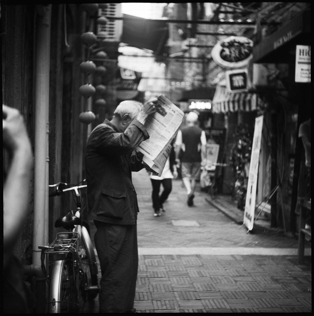 Grayscale Photo of Person Standing While Holding a Newspaper